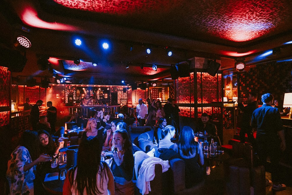 Guests at lounge tables inside Coya Club Marbella at Puente Romano, lit red and blue