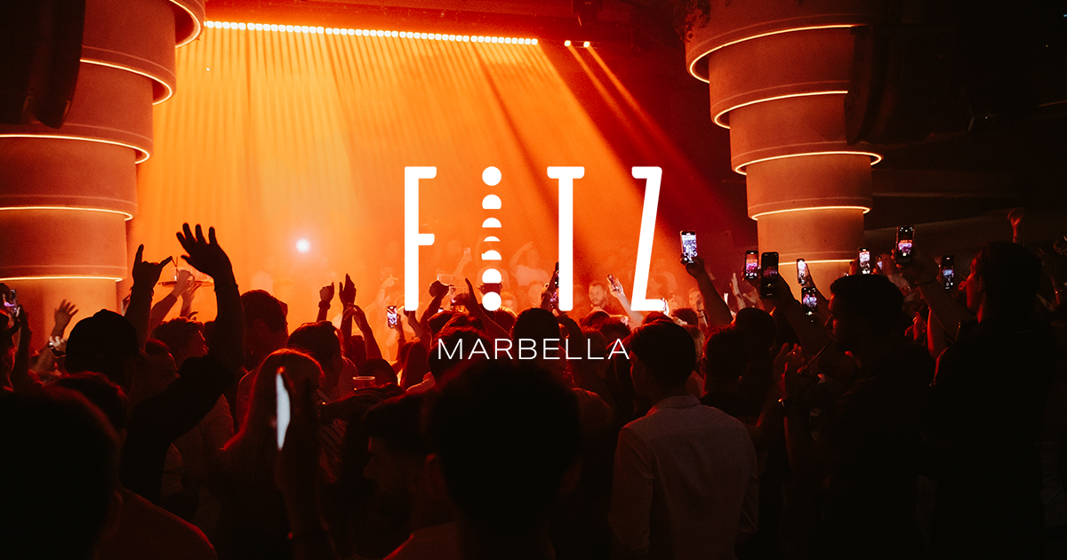 Crowd with hands raised on the main dance floor at Fitz Marbella nightclub in Puerto Banús, lit orange