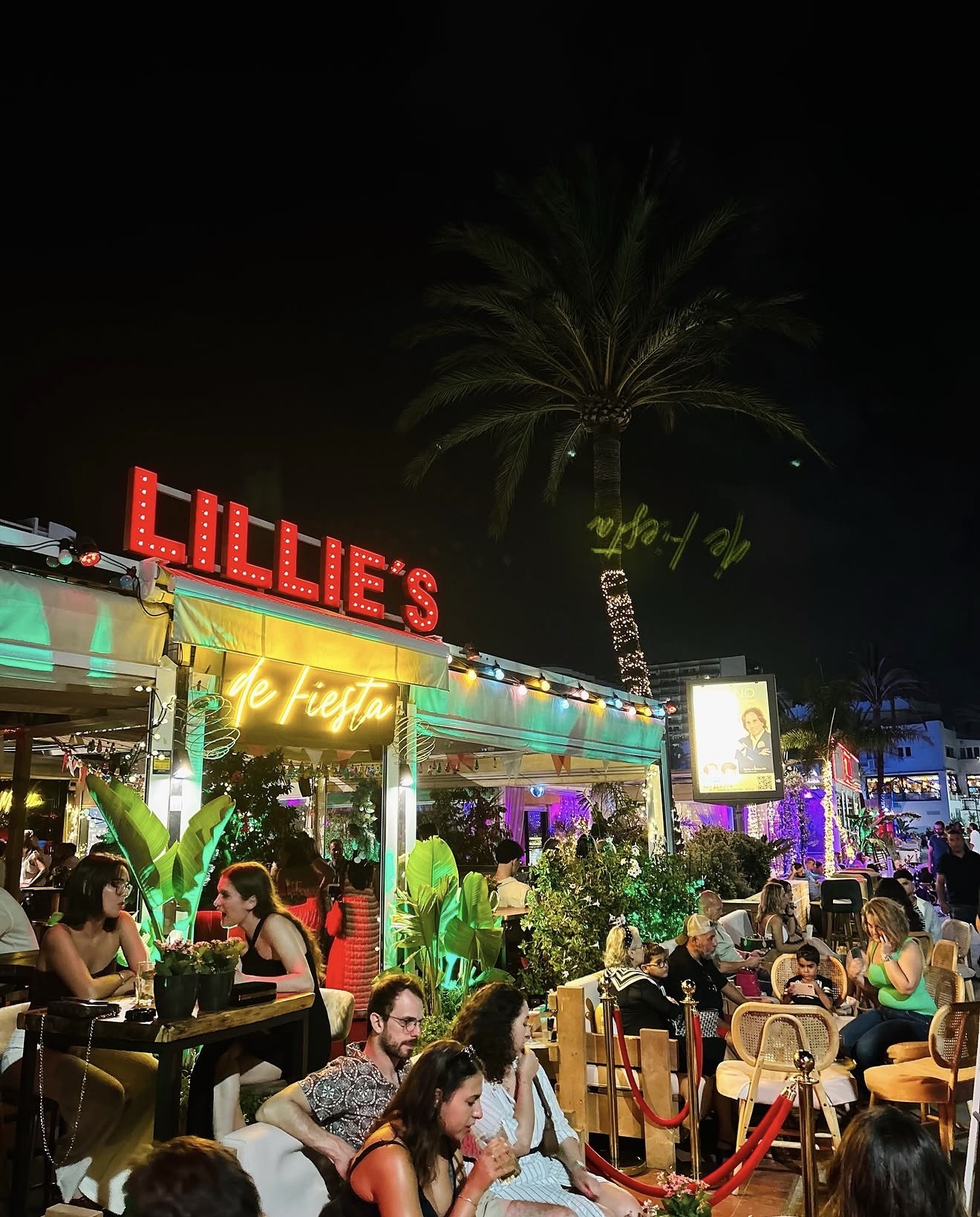 Lillie's Marbella terrace at night, guests seated at tables beneath a palm tree and string lights
