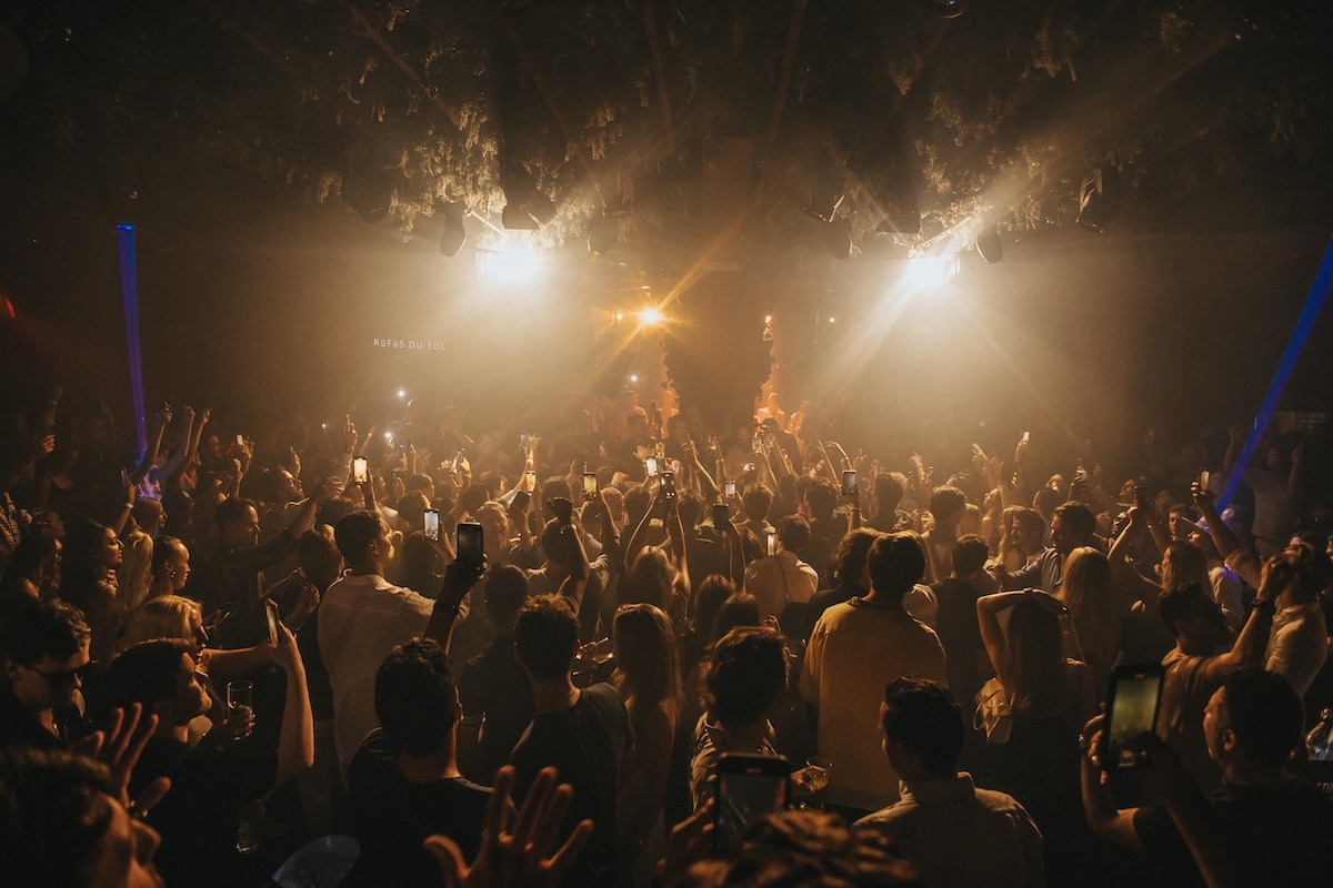 Packed dance floor at Momento Marbella, crowd with phones up as the DJ plays under white beams